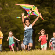 Large group of joyful kids running with a kite in springtime.